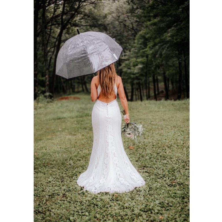 Bride holding a parasol and bouquet with her back to the camera.